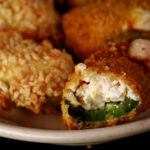 A close up view of air fryer gluten-free jalapeno poppers. One has a bite taken out of it.