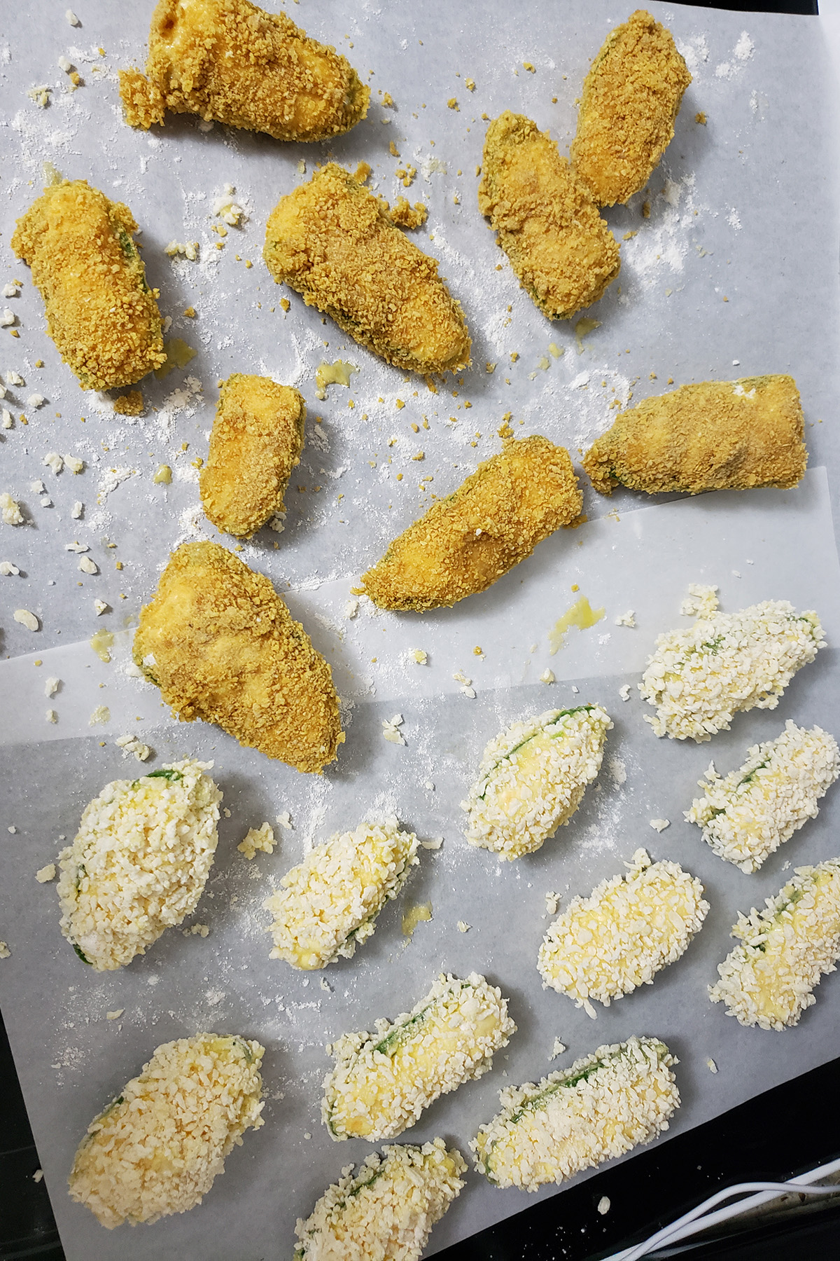 Jalapeno poppers have been coated in two different fillings and arranged on parchment paper.