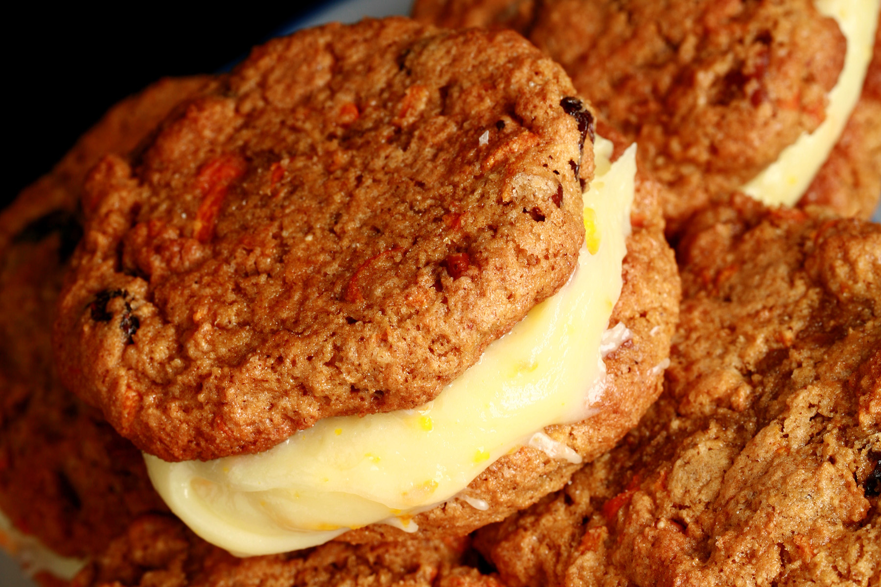A small blue and white plate with a stack of gluten-free carrot cake cookies on it. The filling is ivory coloured and has flecks of orange zest throughout