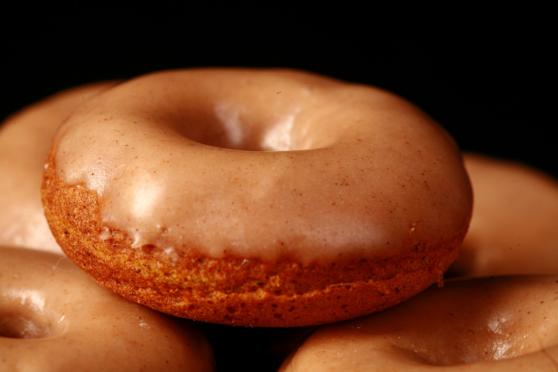 Close up view of gluten-free pumpkin spice mini doughnuts. They are glazed with a tan coloured frosting.