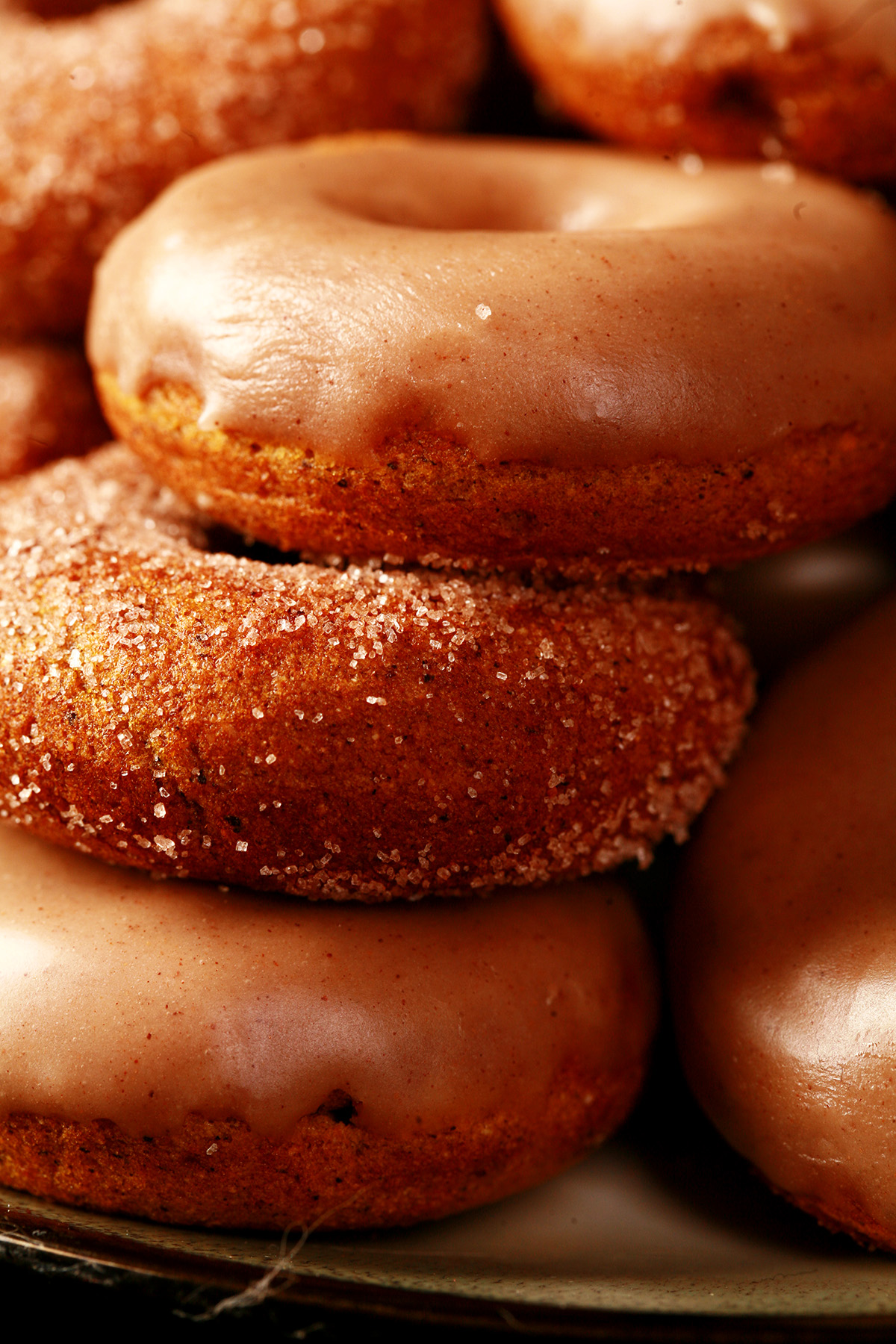 Close up view of gluten-free pumpkin spice mini doughnuts. Some are coated in cinnamon sugar, others are glazed with a tan coloured frosting