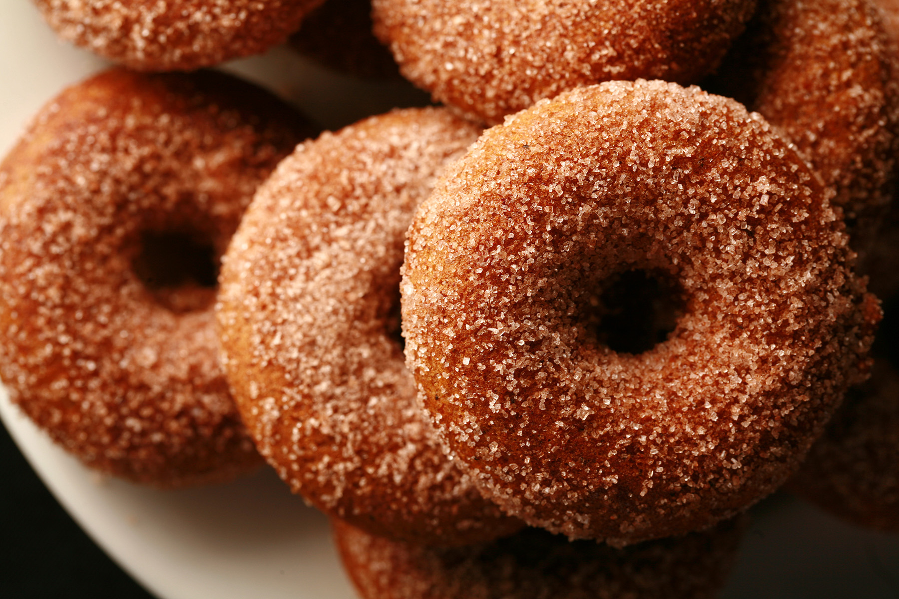 "Close up view of gluten-free pumpkin spice mini doughnuts, coated in cinnamon sugar