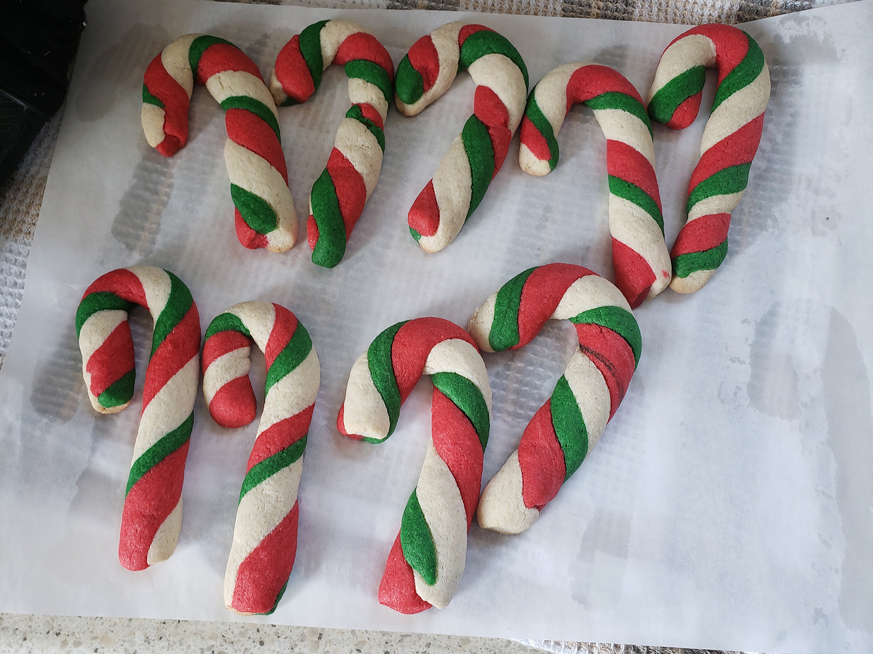 Candy cane shaped cookies made of red, white, and green dough are resting on parchment paper.