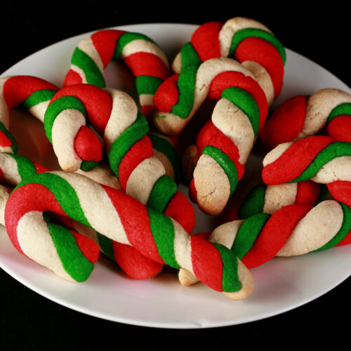 Gluten-Free Candy Cane cookies - candy cane shaped cookies, made from lengths of red, green, and white twisted dough - on a plate.