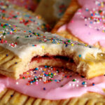 A plate of homemade gluten-free pop tarts, frosted with pink and white icing, topped with coloured sprinkles.