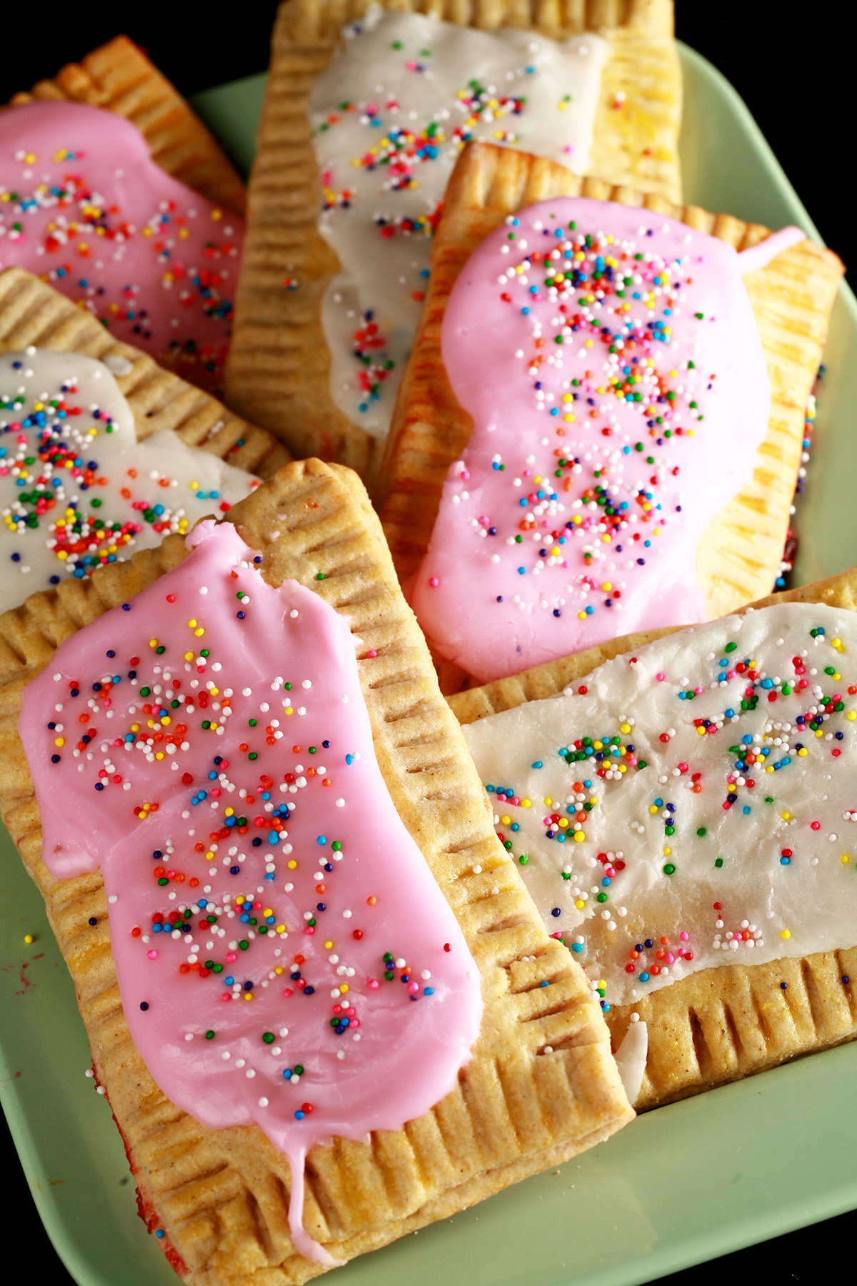 A plate of toaster pastries made from this gluten-free poptarts recipe. They are frosted with pink and white icing, and topped with coloured sprinkles.