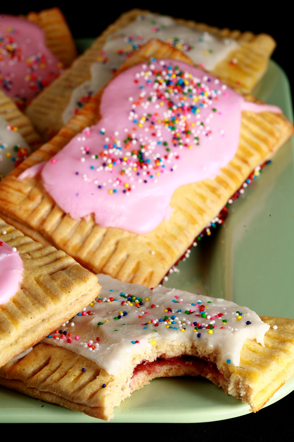 A plate of homemade gluten-free poptarts, frosted with pink and white icing, topped with coloured sprinkles.