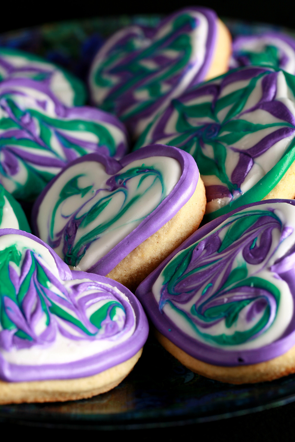 Close up view of a plate of heart shaped cookies decorated with swirls of teal and lavender over white.