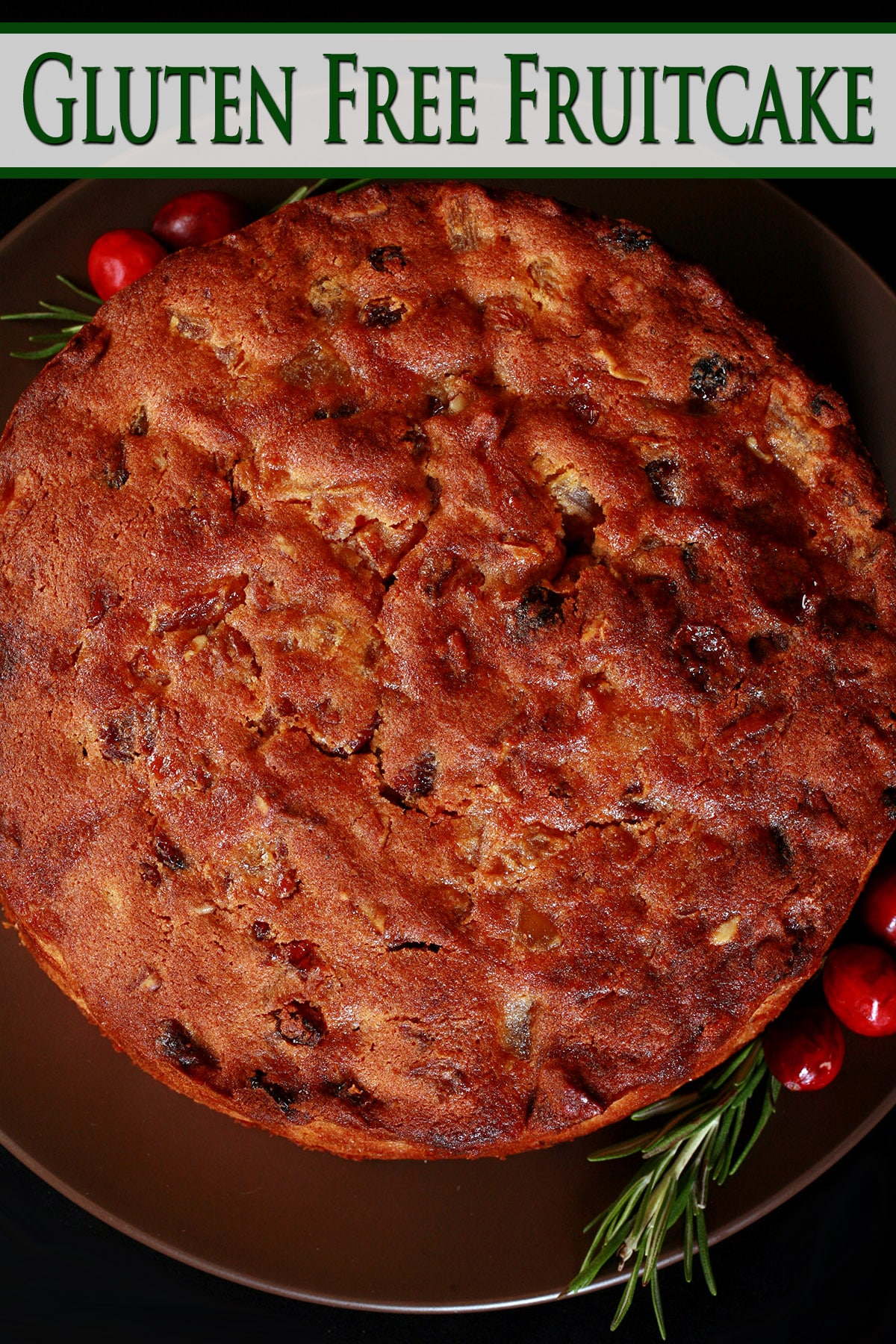 A whole gluten free fruitcake, with rosemary and cranberries beside it.