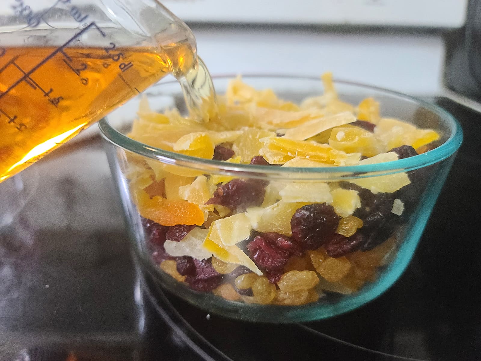 Whiskey being poured over the bowl of dried fruit.