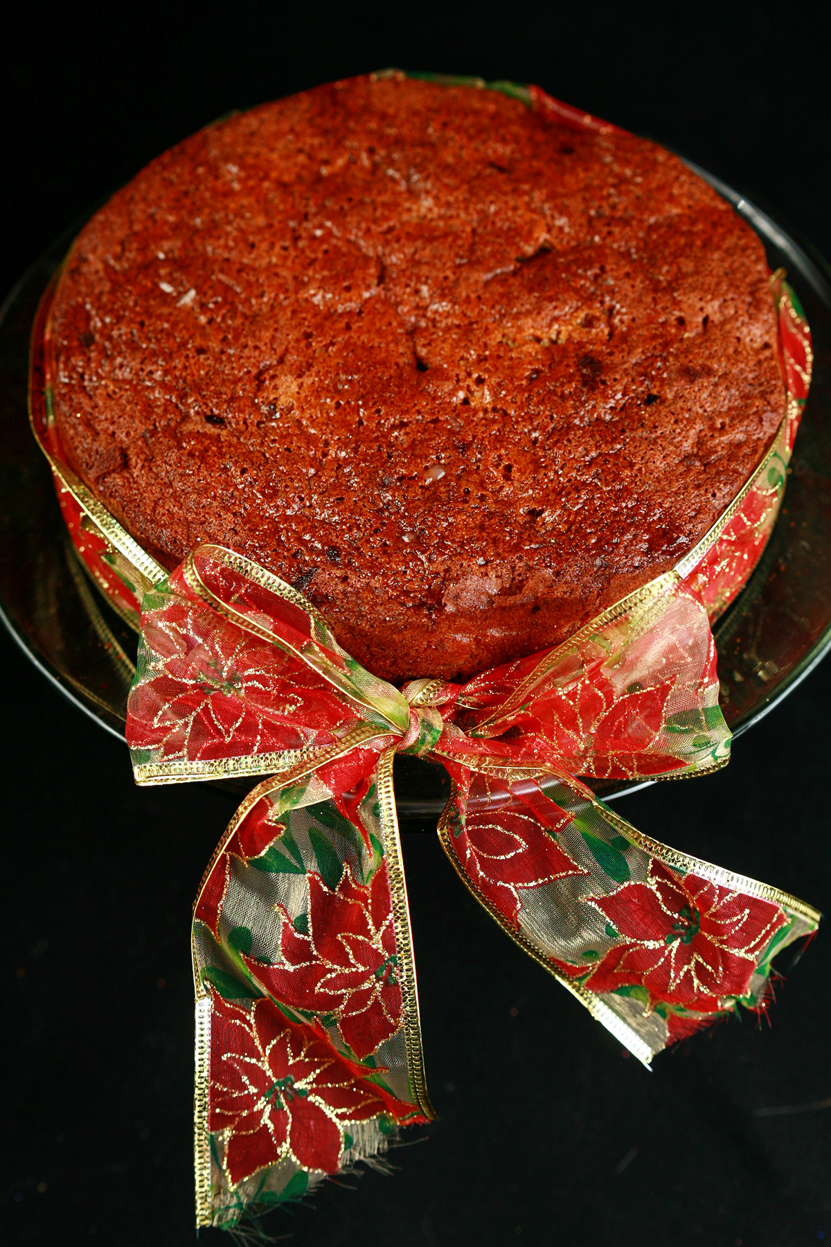 A round fruitcake, tied with a festive red, green, and gold bow.
