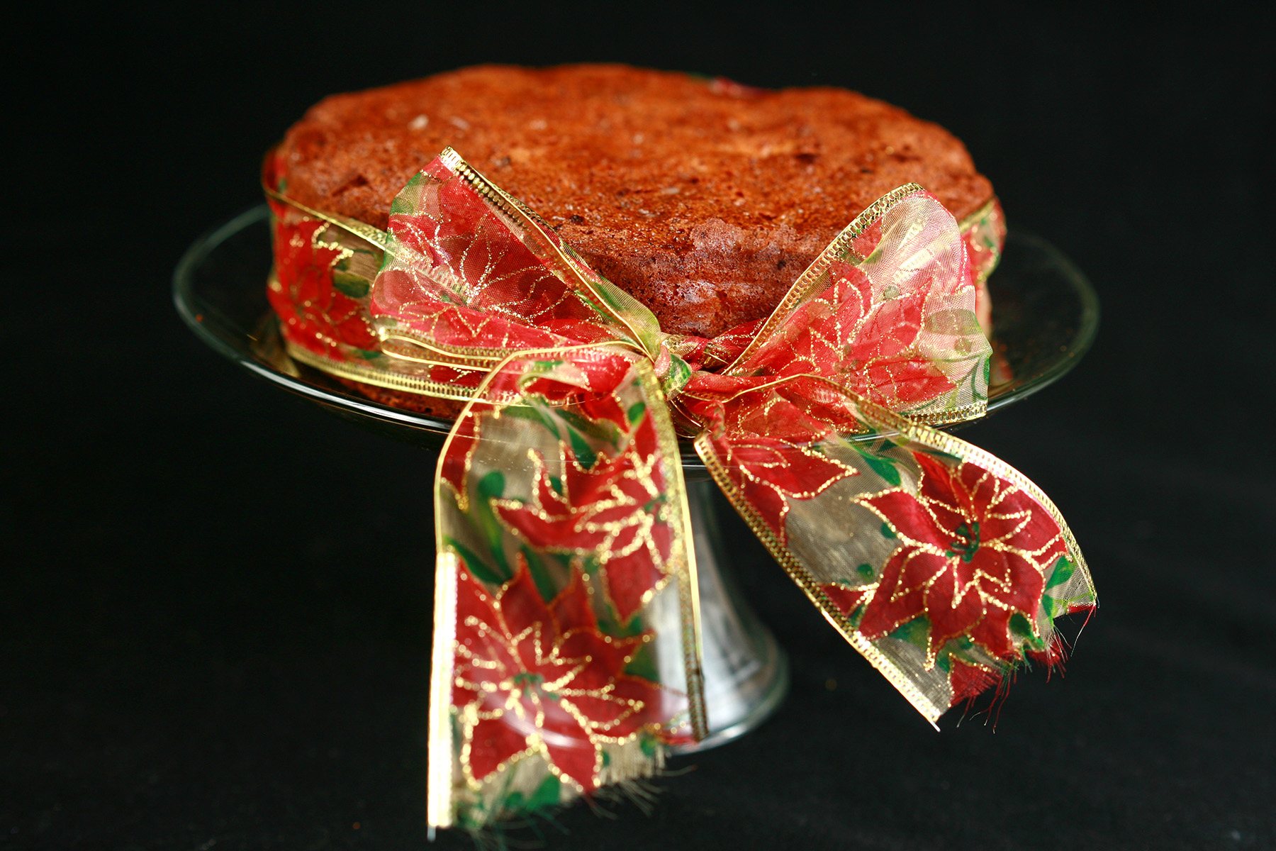 A round fruitcake, tied with a festive red, green, and gold bow.