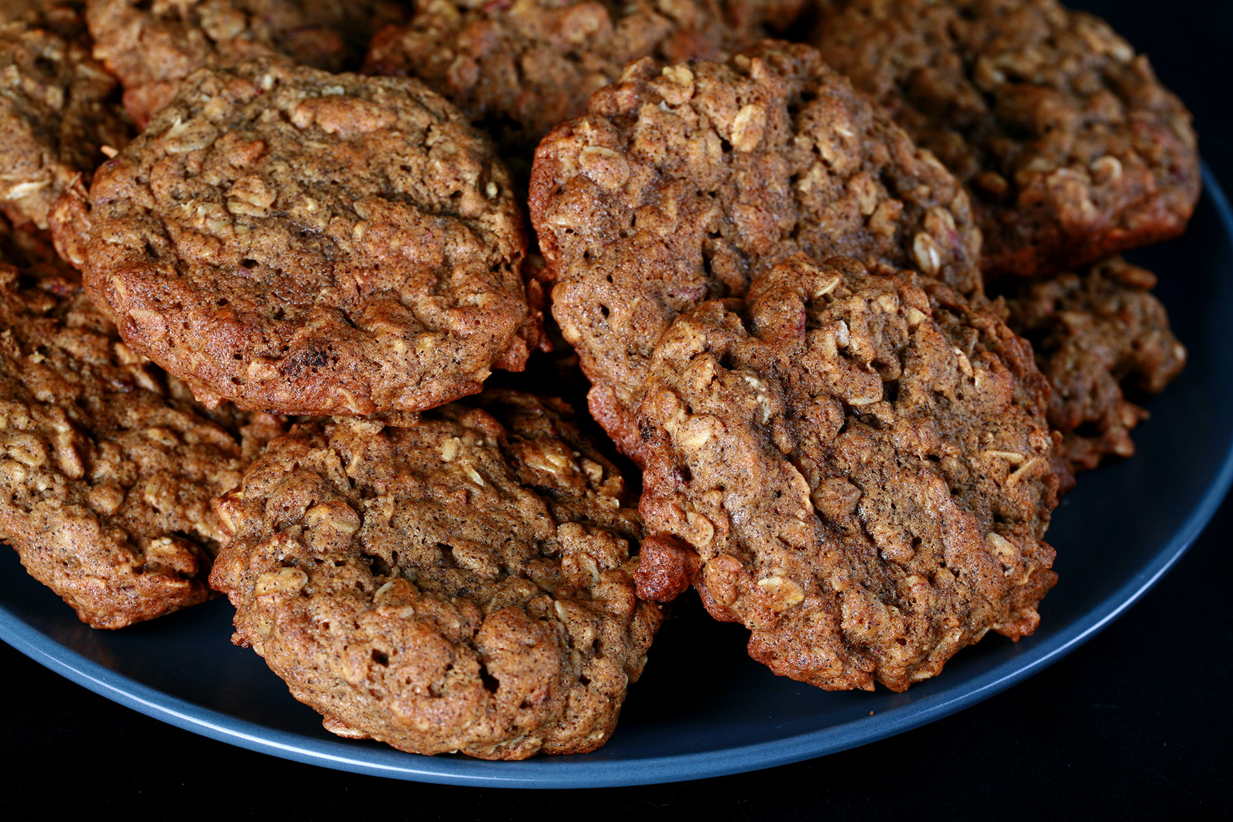 A large blue plate piled with Chewy Gluten-Free Banana Oatmeal cookies, against a black background.