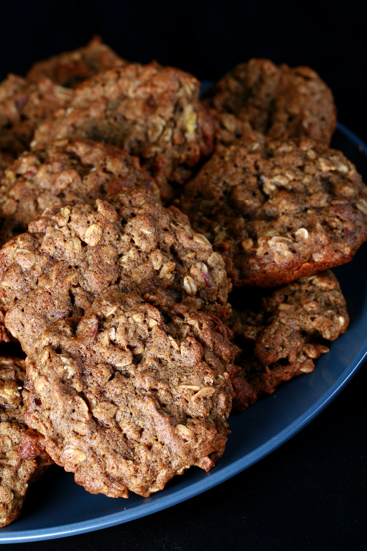 A large blue plate piled with Chewy Gluten-Free Banana Oatmeal cookies, against a black background.