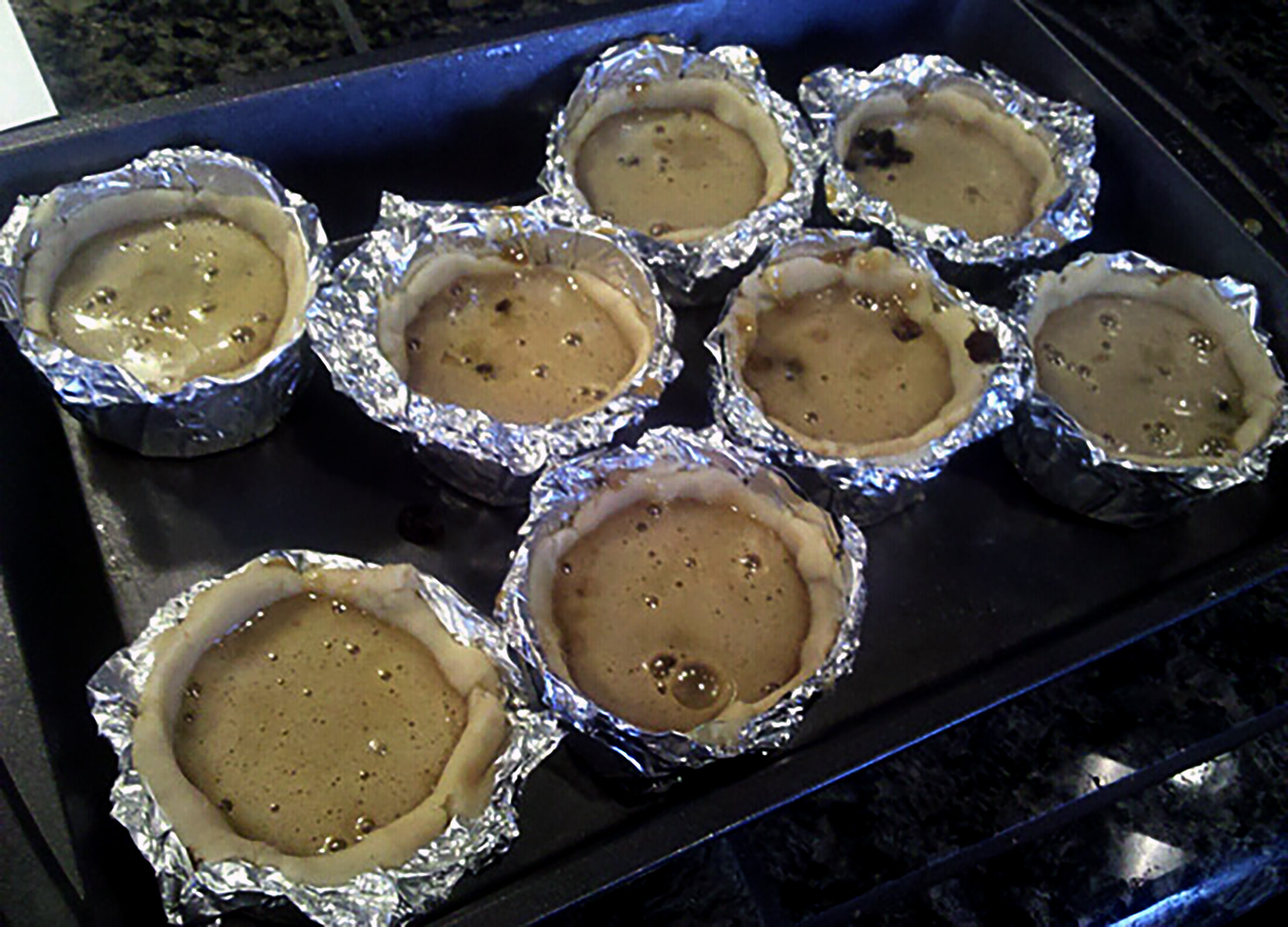Homemade foil cuts, arranged in baking pans.  The cups have been lined with dough and filled with raisings and filling.