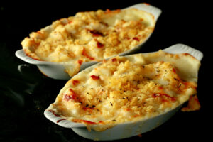 Two oblong ceramic ramekins of gluten-free cod au gratin. Cod is in a creamy, cheesy sauce, topped with crushed chips, more cheese, and savoury.