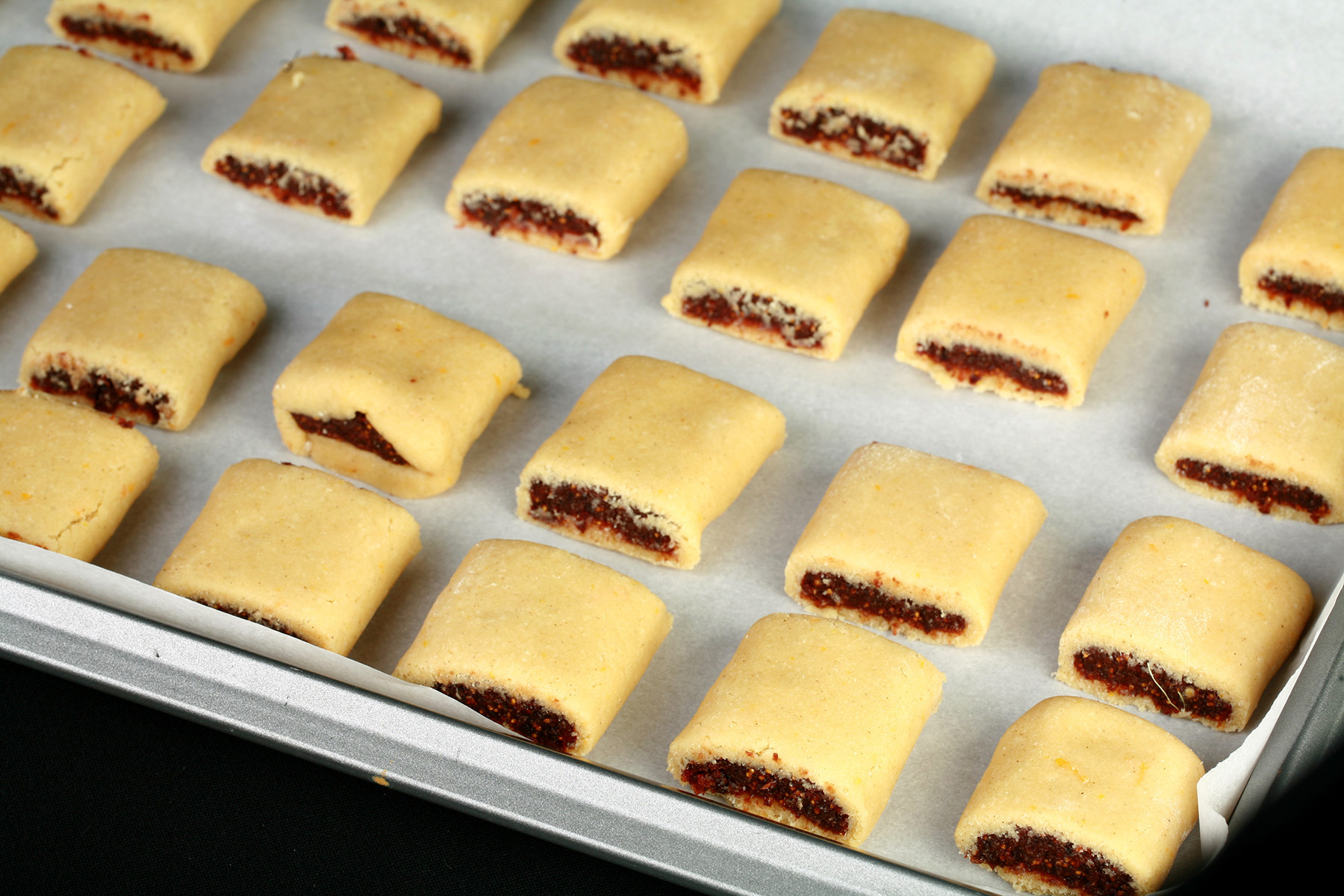 Rows of raw fig newton cookies, lined up on a parchment lined baking sheet.