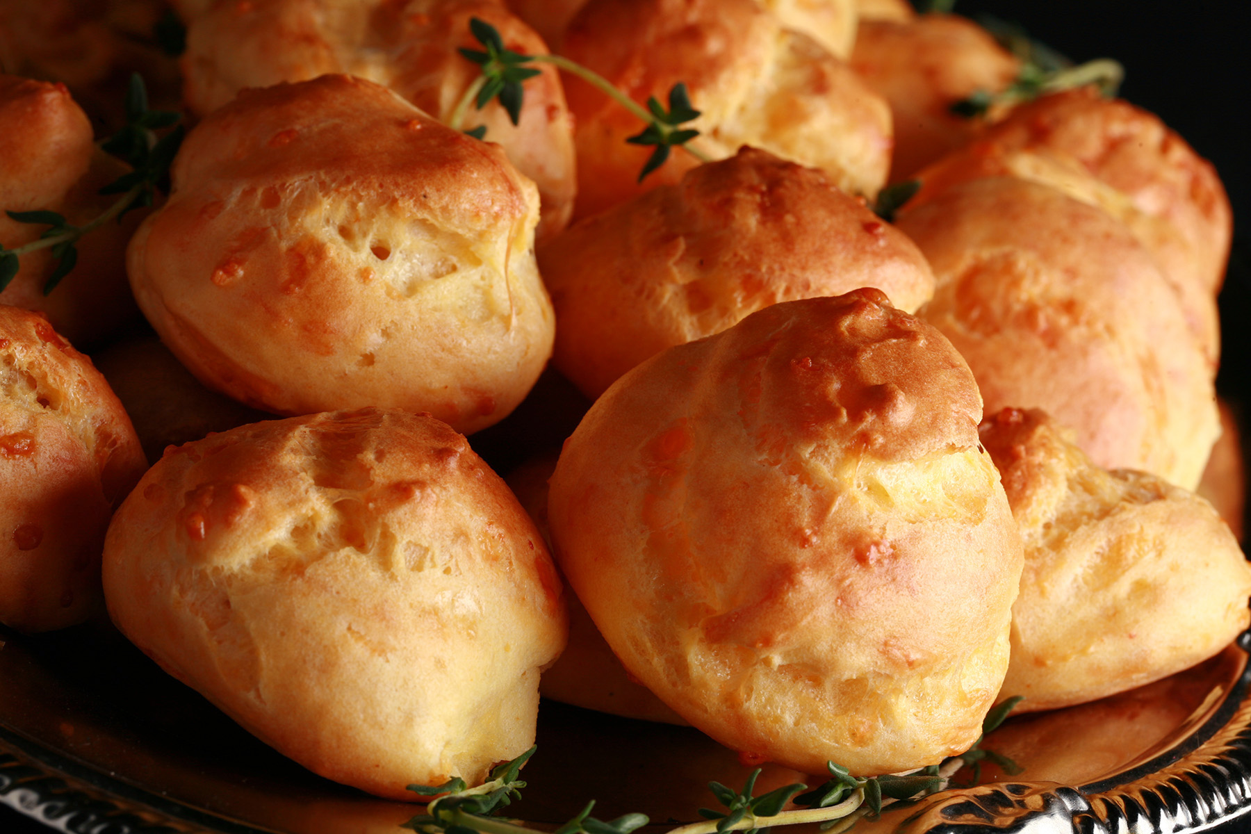 A large pile of Gluten-free Cheese Puffs - small, cheesy pastries - on a silver plate.