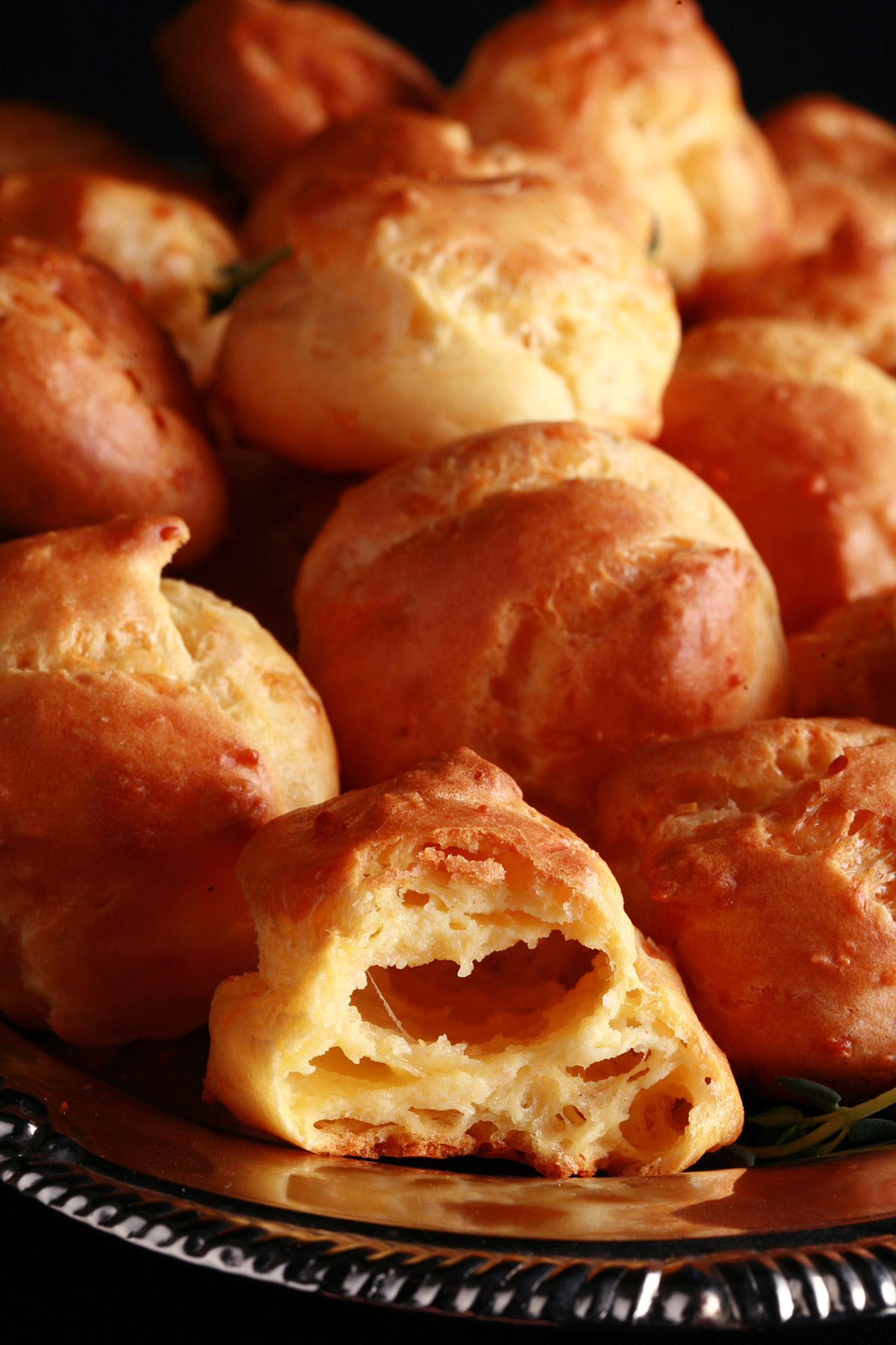 A large pile of Gluten-free Gougères - small, cheesy pastries - on a silver plate.