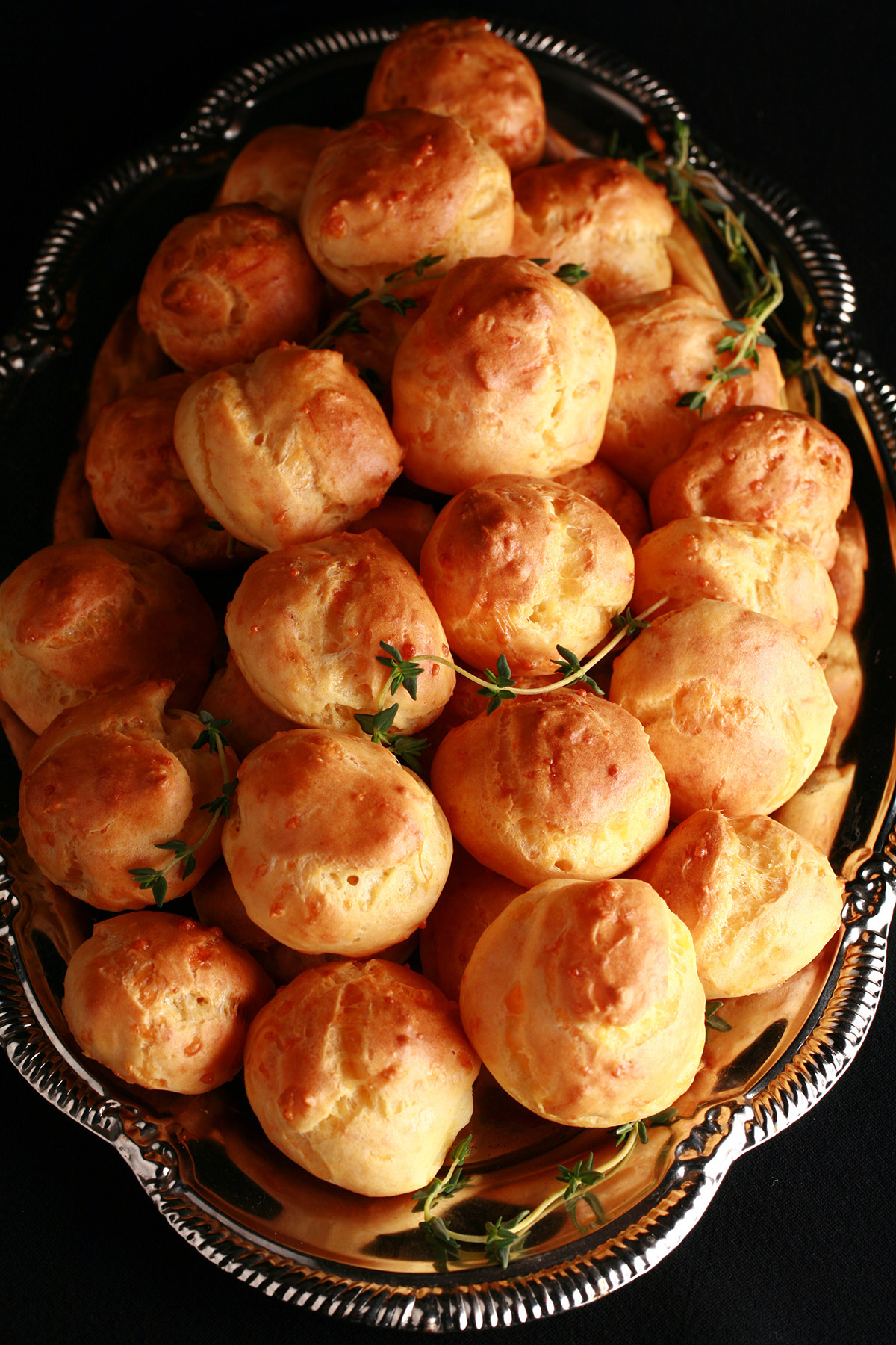 A large pile of Gluten-free Gougères - small, cheesy pastries - on a silver plate.
