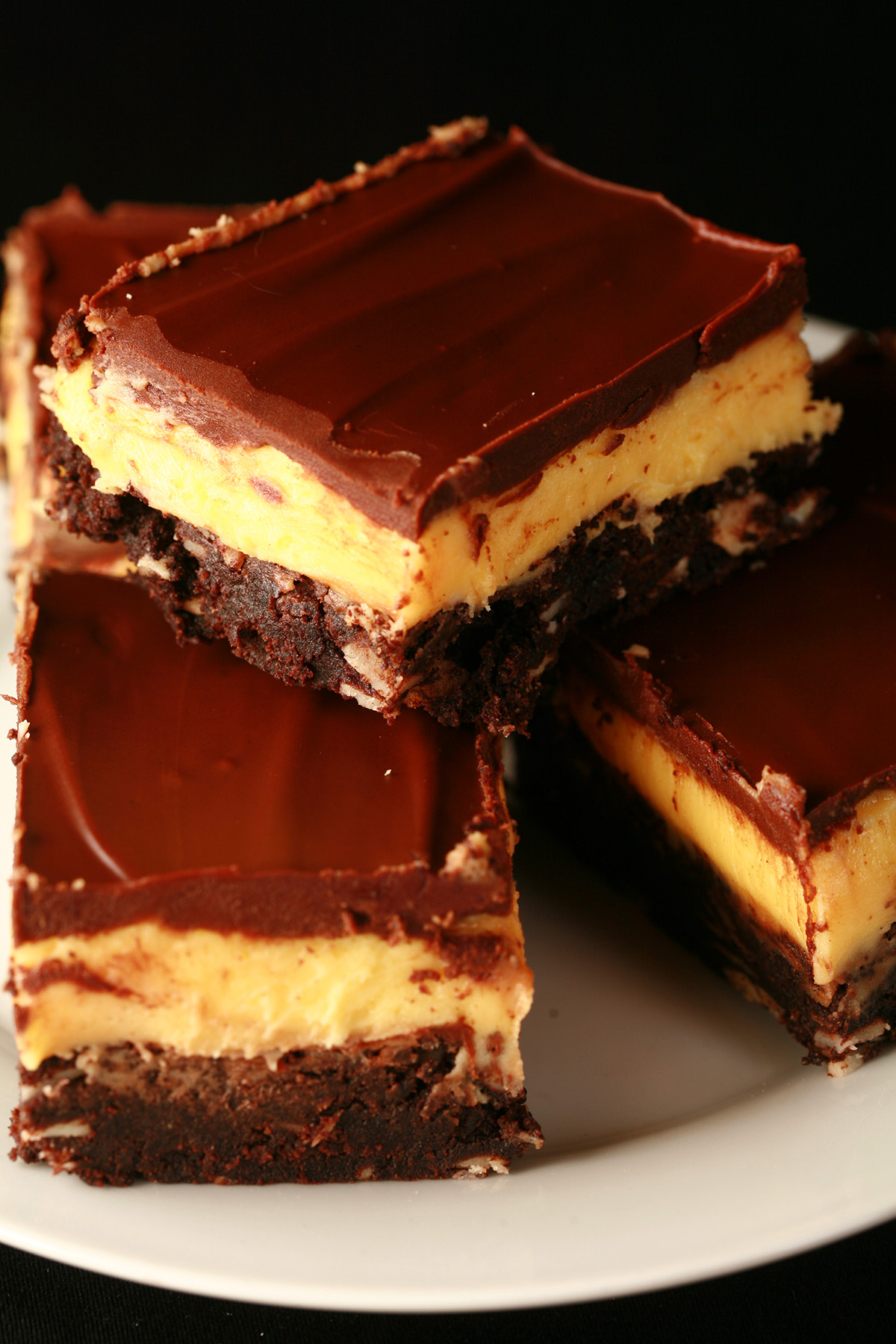 A plate of gluten-free Nanaimo Bar Brownies - A fudgey brownie, topped with a rich custard buttercream and a layer of chocolate ganache.