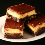A plate of gluten-free Nanaimo Bars - A fudgey brownie, topped with a rich custard buttercream and a layer of chocolate ganache.