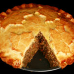 A golden brown gluten-free tourtiere meat pie, with a maple leaf design on top.. There is a section cut out of it