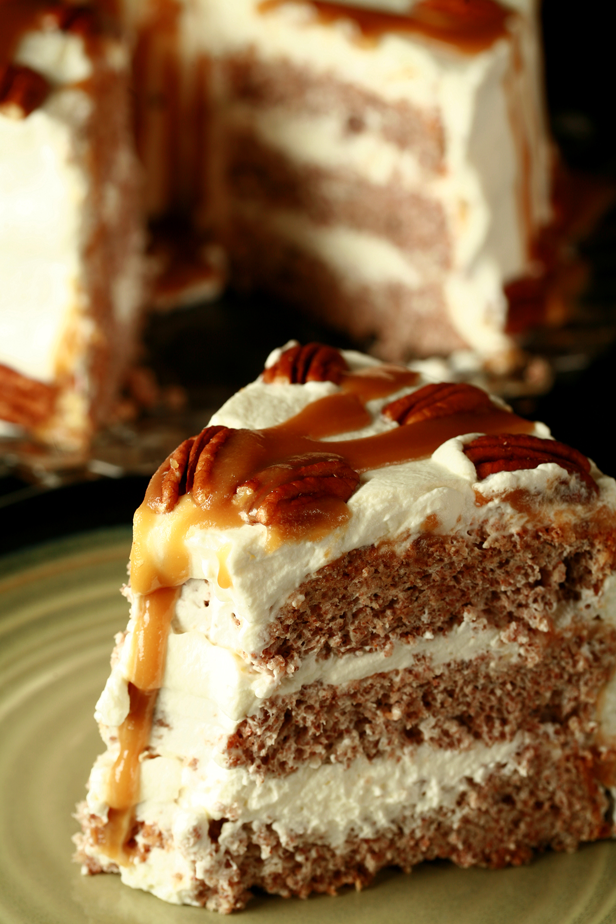 A close up view of a schmoo torte - layers of pecan angel food cake and whipped cream, topped with pecans and with caramel sauce drizzled all over it!