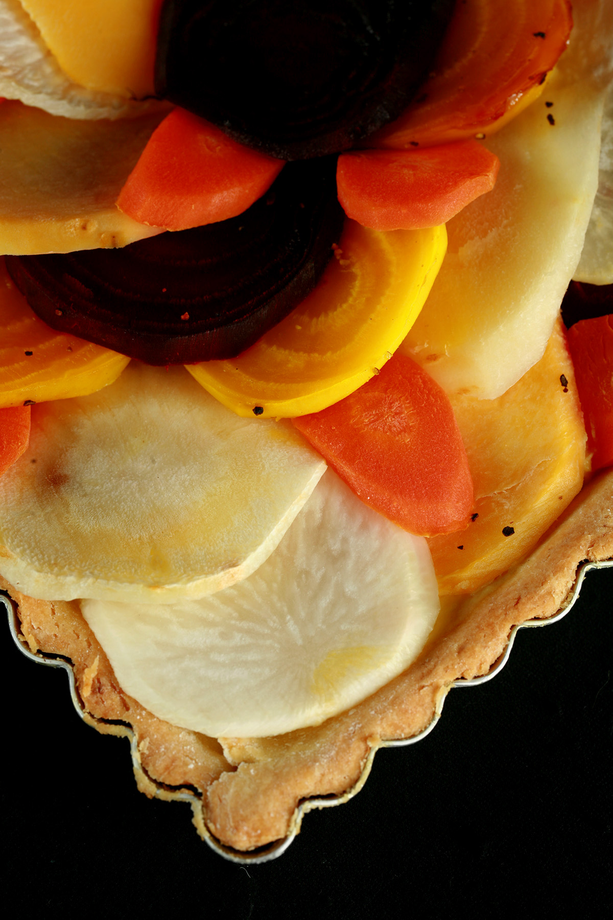 A close up view of a square root tart - a tart cooked in a square pan, with slices of a variety of root veggies arranged on top.