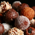 A close up view of an assortment of gluten-free doughnut holes: Toasted coconut, chocolate glazed, cinnamon sugar, powdered sugar, and dutchie versions are all visible.