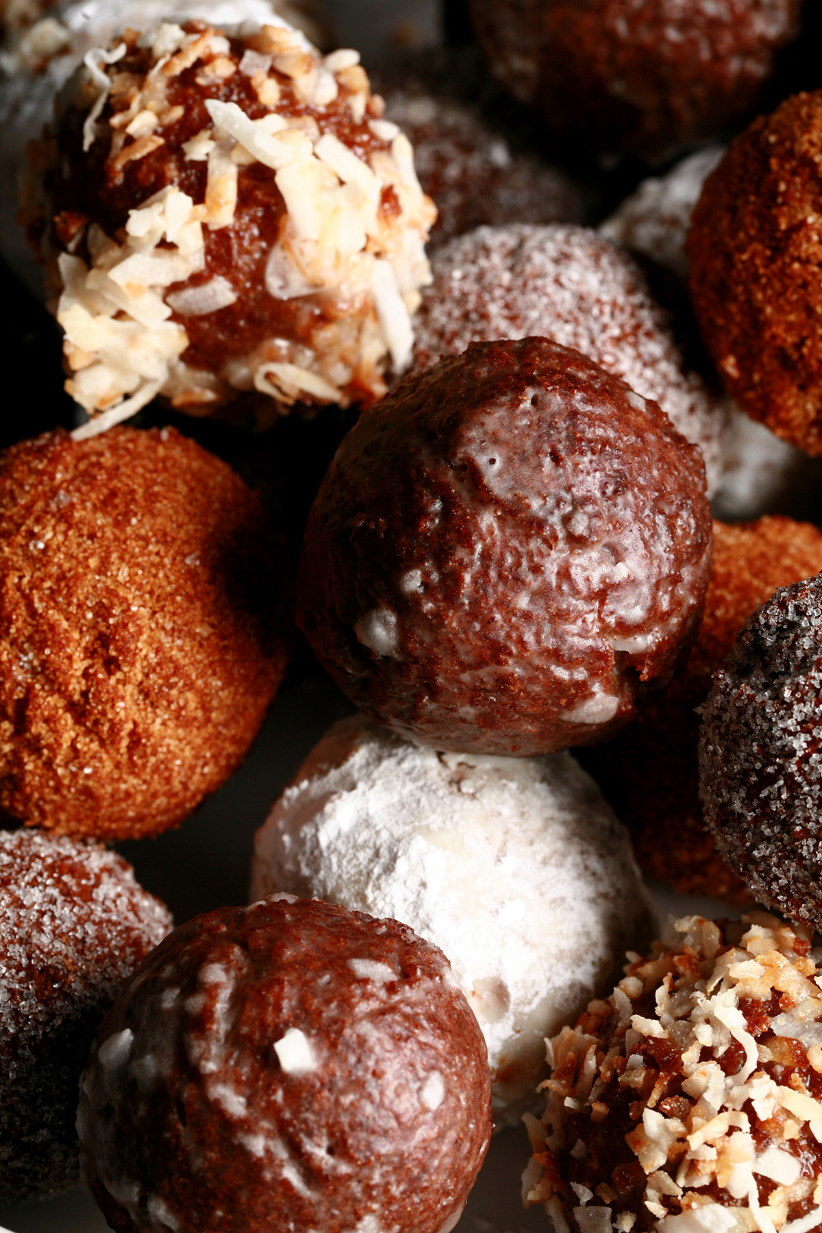 A close up view of an assortment of gluten-free timbits: Toasted coconut, chocolate glazed, cinnamon sugar, powdered sugar, and dutchie versions are all visible.