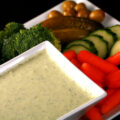 A bowl of AIP Ranch dressing, surrounded by cut vegetables.