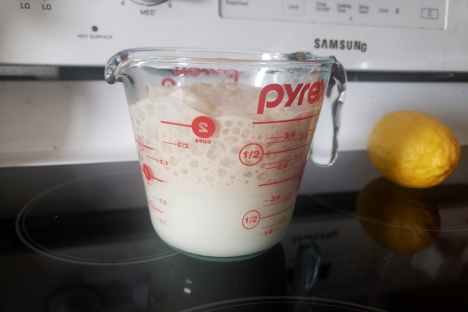 A measuring cup half full of milk. The top is frothy from proofing yeast.
