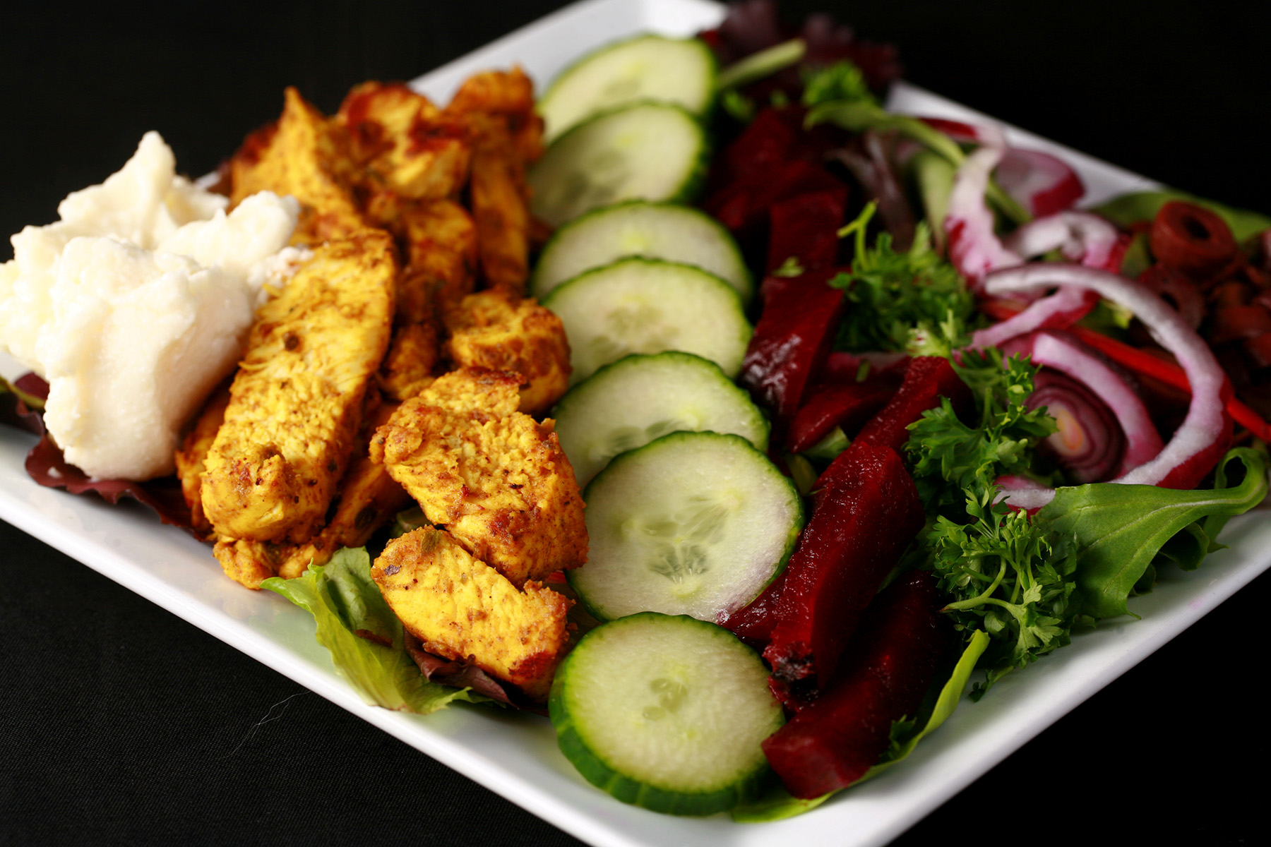 An AIP chicken shawarma salad, with stripes of chicken, pickled beets, cucumbers, red onions, and toum.