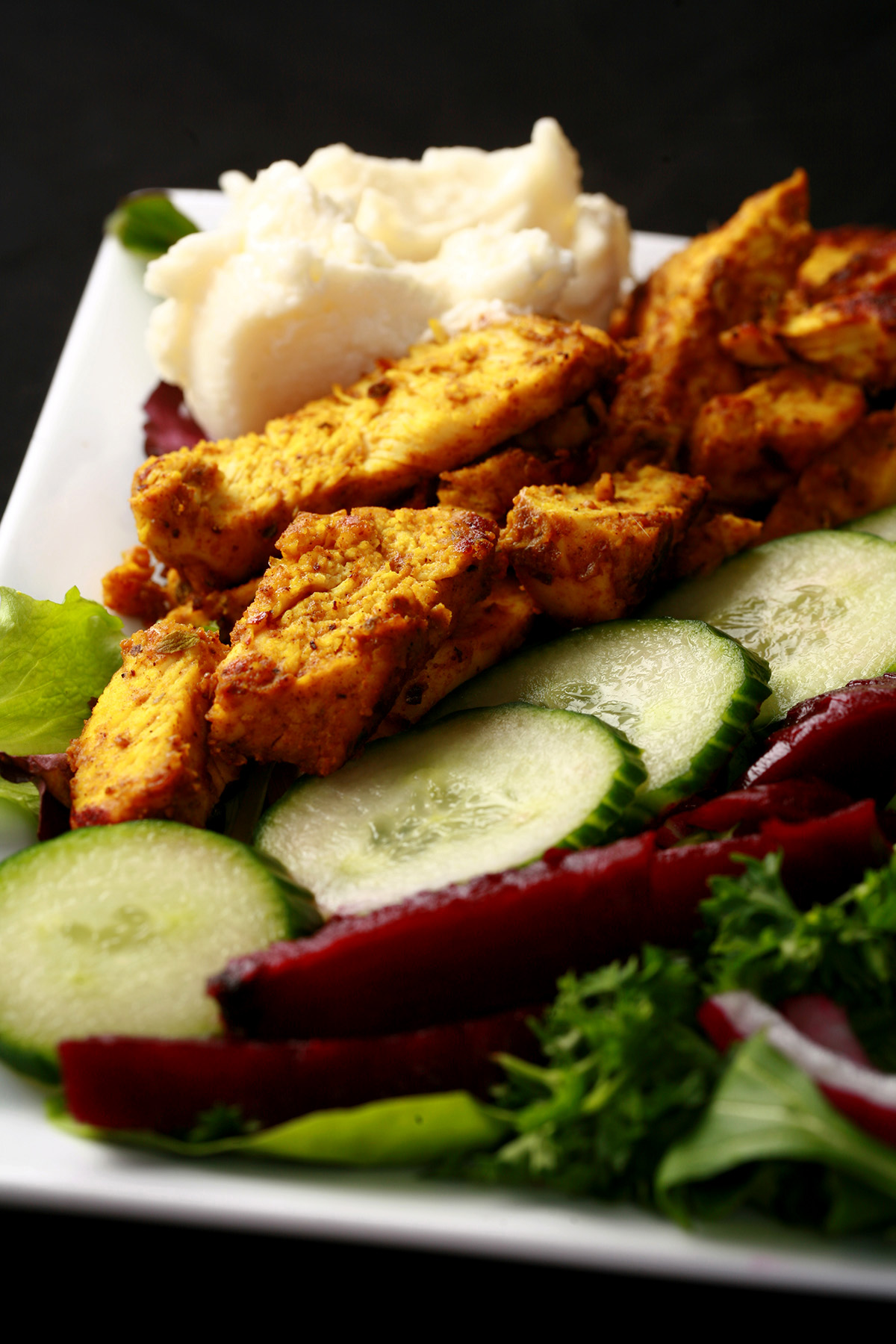 An AIP chicken shawarma salad, with stripes of chicken, pickled beets, cucumbers, red onions, and toum.