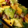 A close up view of a bowl of chunky mango salsa. Mango, avocado, red onion, and cilantro are all visible.