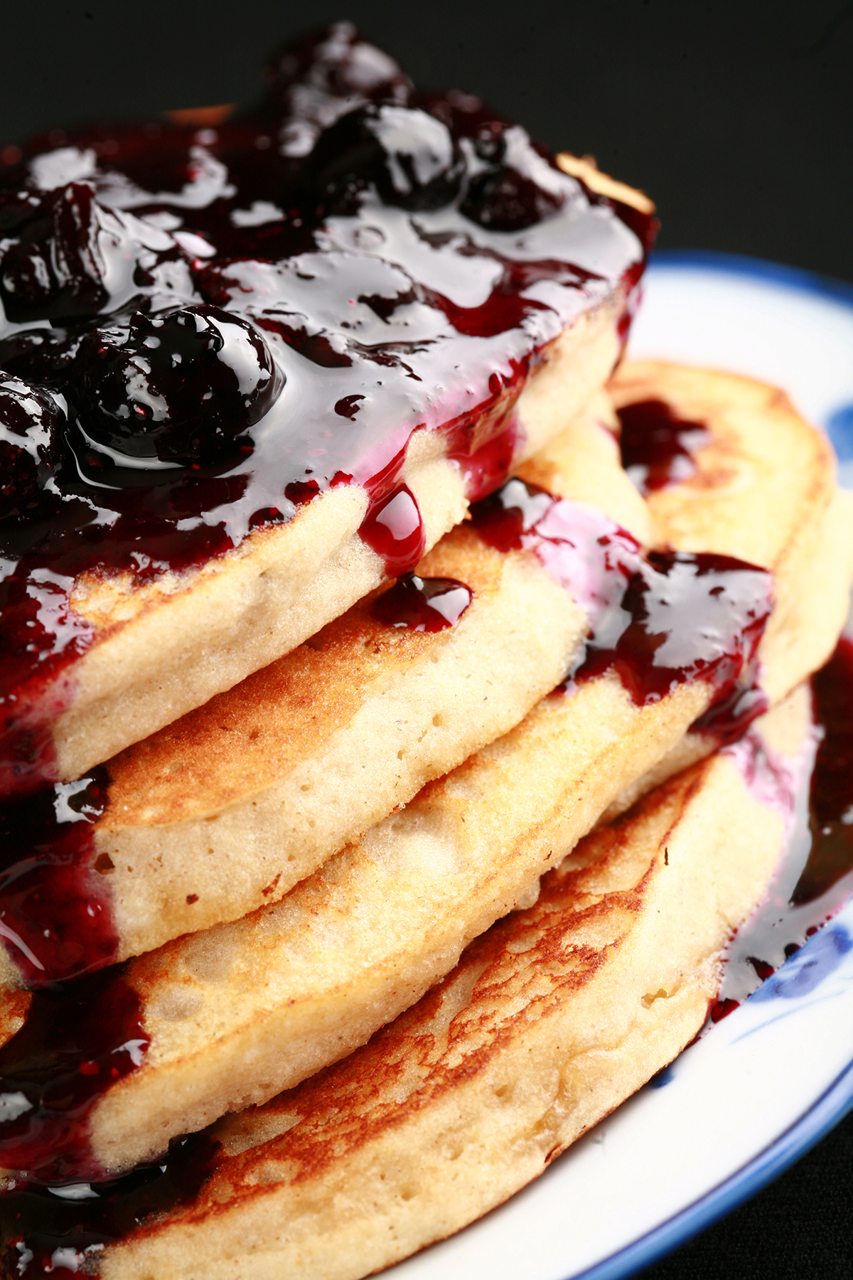 A stack of gluten-free banana buckwheat pancakes on a plate. It is topped with fresh blueberry sauce.