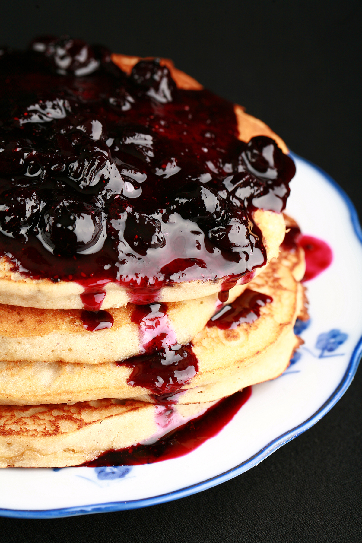 A stack of gluten-free banana buckwheat pancakes on a plate. It is topped with fresh blueberry sauce.