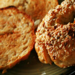A close up view of two toasted gluten-free bagels on a plate. One is coated with everything seasoning.