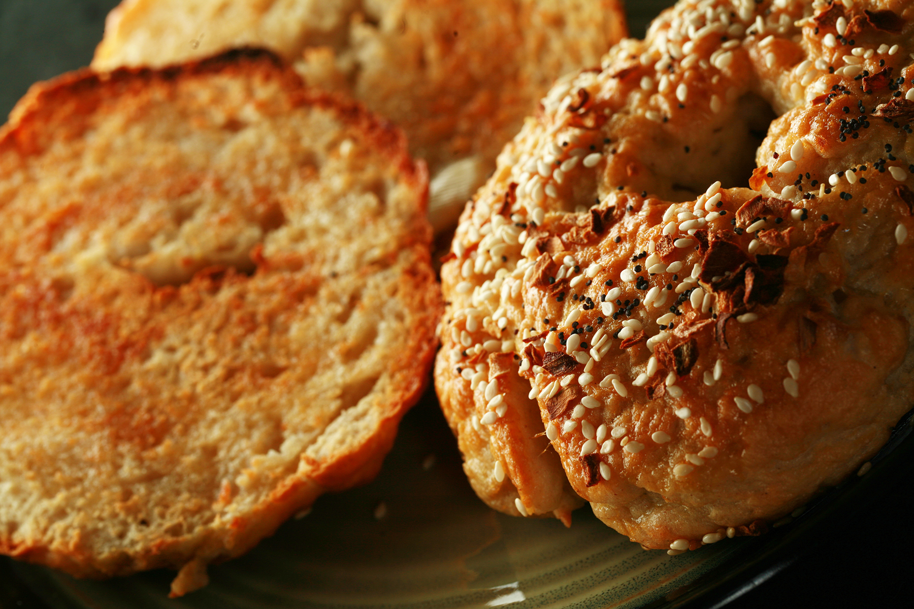 A close up view of two toasted gluten-free bagels on a plate. One is coated with everything seasoning.