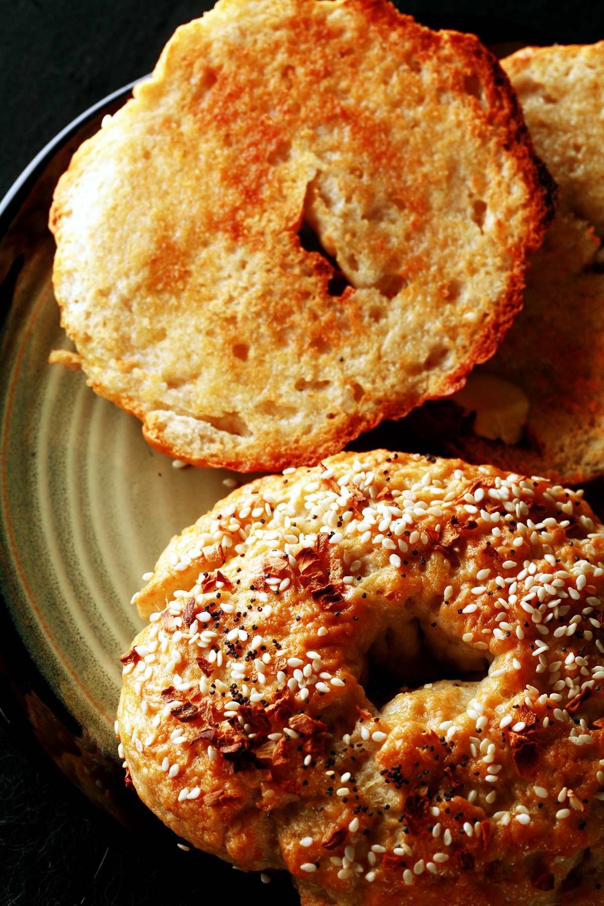 A close up view of two toasted gluten-free bagels on a plate. One is coated with everything seasoning.