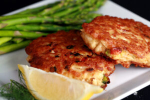 2 Gluten-free Crab Cakes on a plate with asparagus, a lemon slice, and some fresh dill.