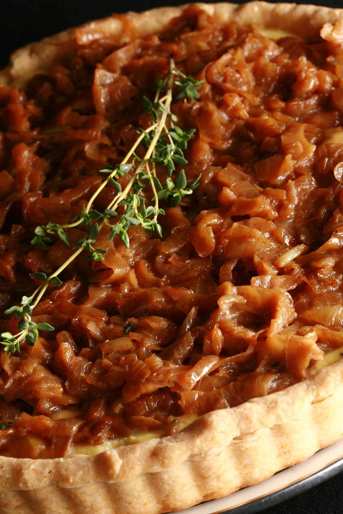 A close up view of a gluten-free French onion soup tart. The top is covered in caramelized onions and garnished with thyme.