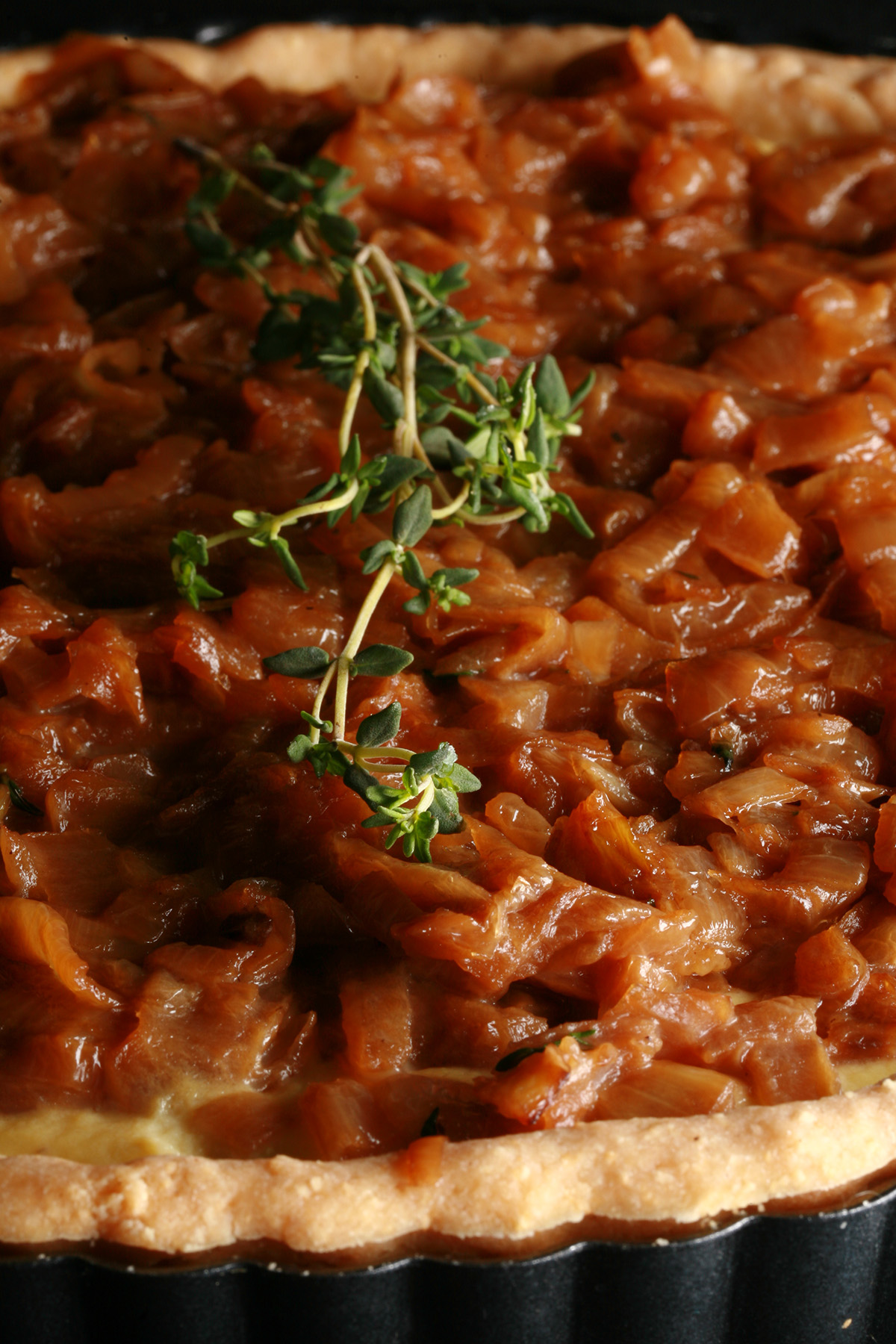 A close up view of a gluten-free French onion soup tart. The top is covered in caramelized onions and garnished with thyme.