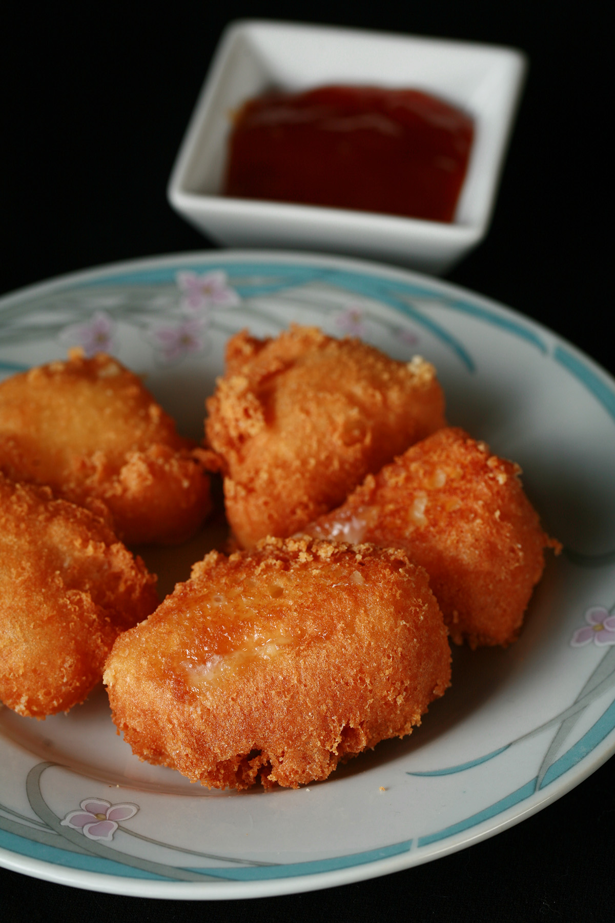 Several small wedges of gluten-free deep fried brie. There is a small bowl of apricot preserves next to the plate.