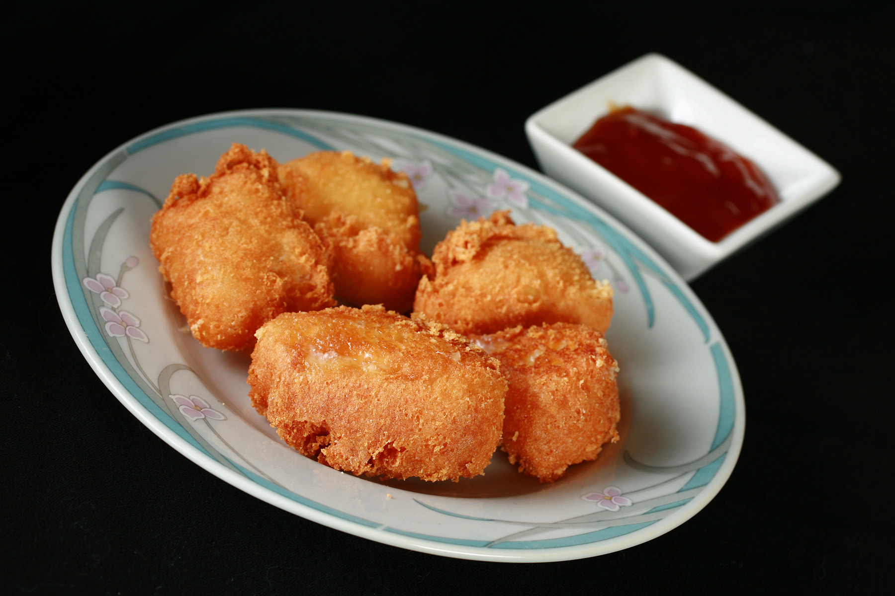 Several small wedges of gluten-free deep fried brie. There is a small bowl of apricot preserves next to the plate.