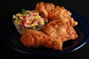 3 pieces of gluten-free fried chicken on a plate, next to a small bowl of colourful coleslaw.