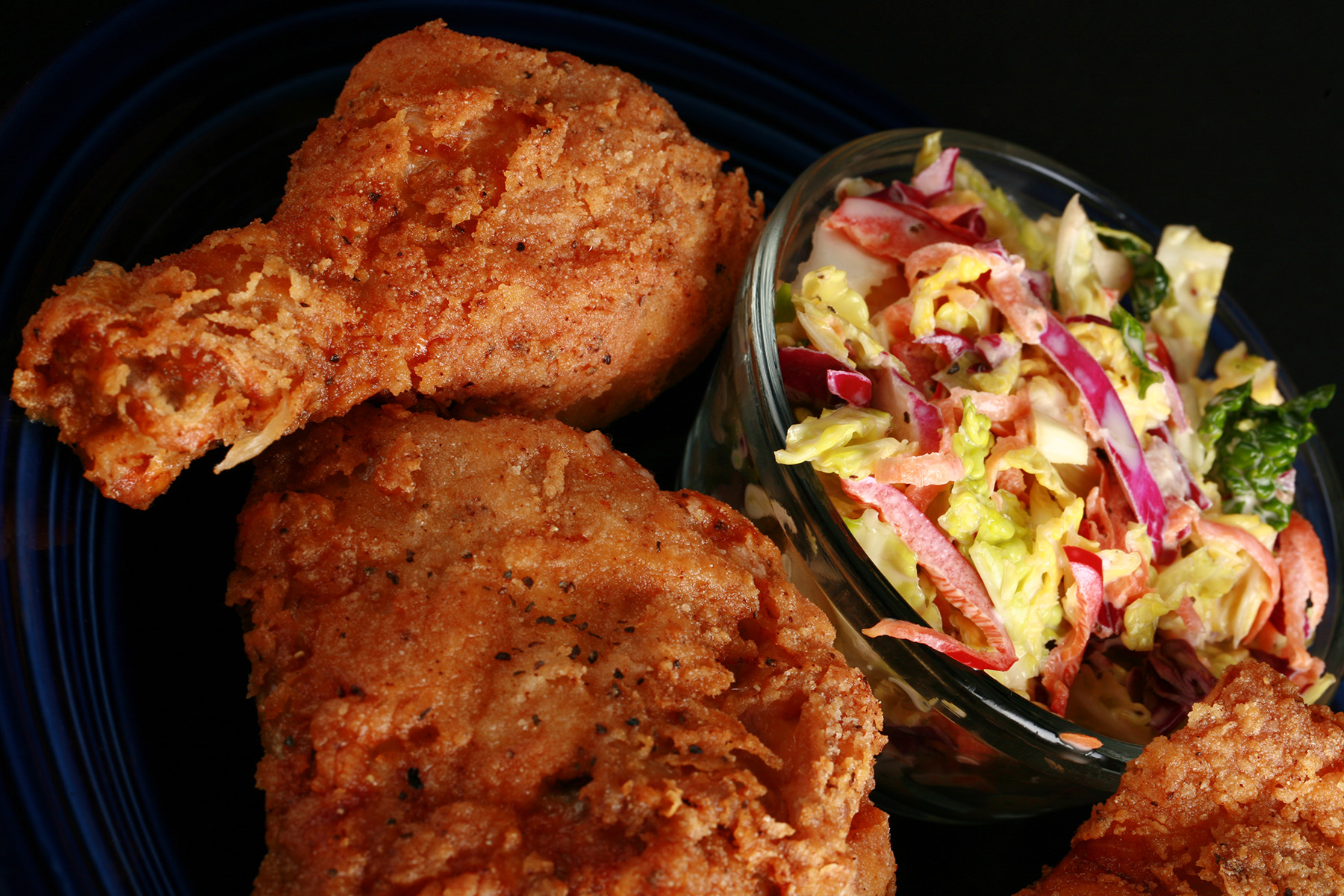 2 pieces of gluten-free fried chicken on a plate, next to a small bowl of colourful coleslaw.