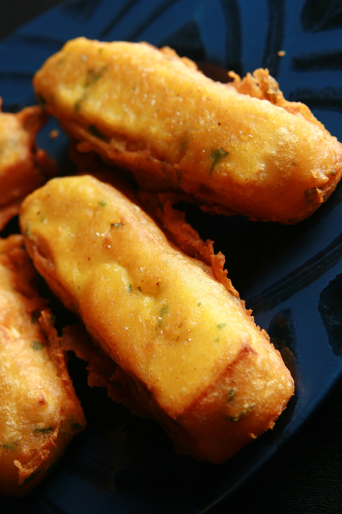 Several sticks of gluten-free paneer pakora - deep fried cheese sticks - on a blue plate.