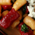 A plate of red and yellow roasted beet gnocchi. It's topped with crumbled goat cheese and fresh basil.